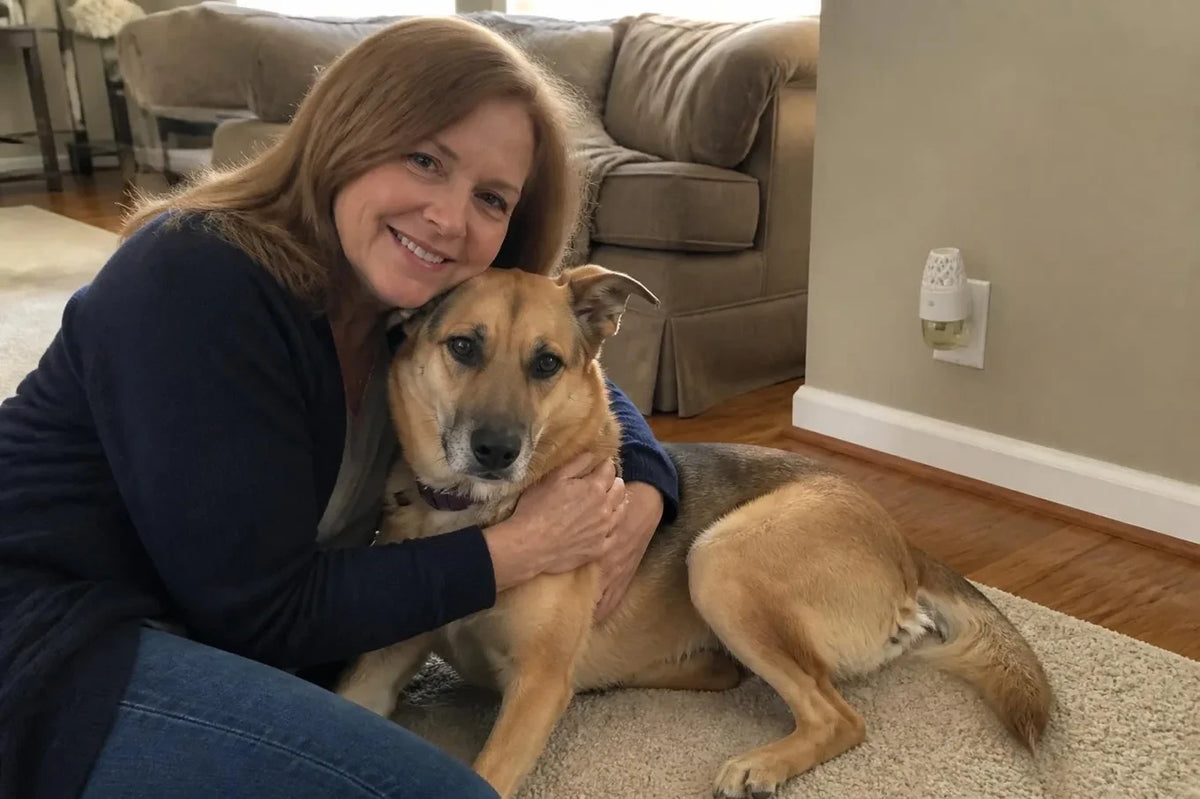 Linda sitting on the clean living room rug hugging Rosie, a plug in diffuser in the wall outlet behind them